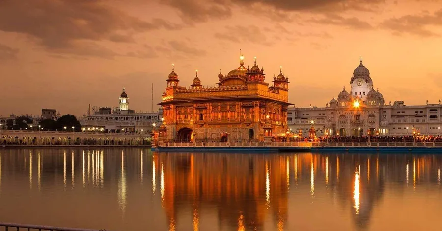 शाम के समय नारंगी रोशनी में चमकता स्वर्ण मंदिर, गर्म शाम के आसमान के नीचे पवित्र सरोवर में उसका प्रतिबिंब